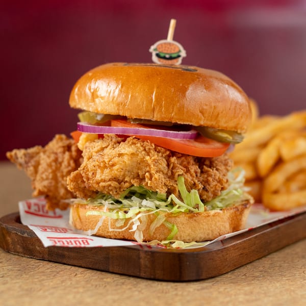 Crispy fried chicken sandwich with lettuce, tomato, onion, and pickles, served with fries.
