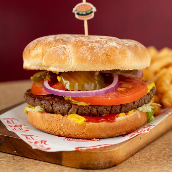 A Bigger Burger with lettuce, tomato, onion, pickles, mustard, and ketchup, with fries in the background.