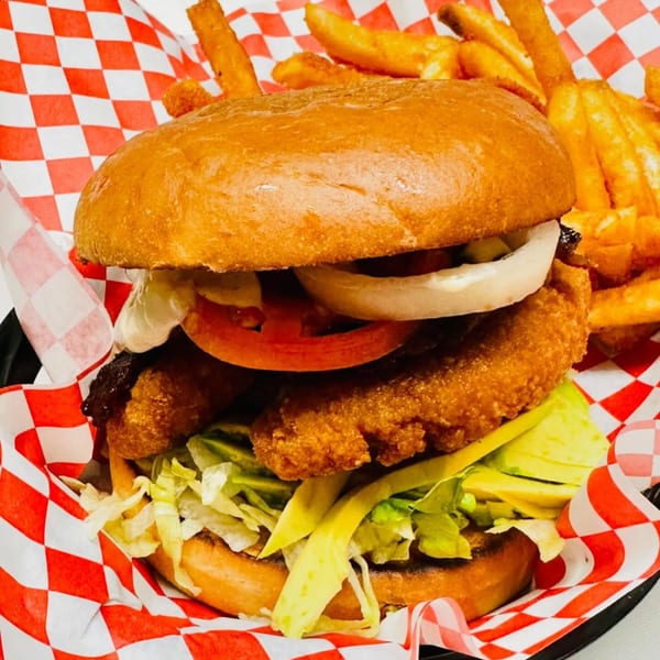 A crispy chicken burger with lettuce, avocado, tomato, onion, and sauce, served with fries.
