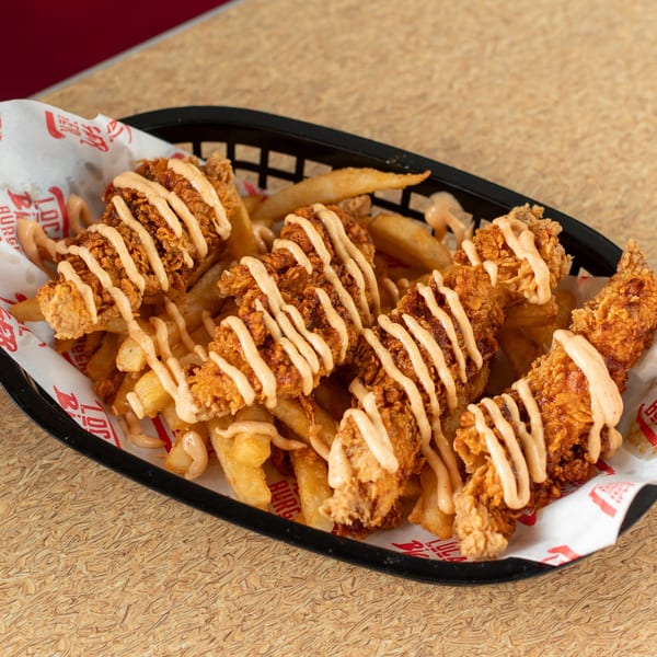 Four crispy chicken tenders drizzled with sauce, served over a bed of fries in a black basket.