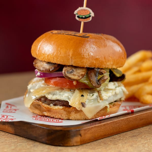 A mushroom burger with melted cheese, red onions, tomatoes, and pickles, served with fries.