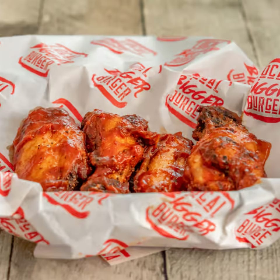 Four barbecue chicken wings in a paper-lined basket from Local Bigger Burger.