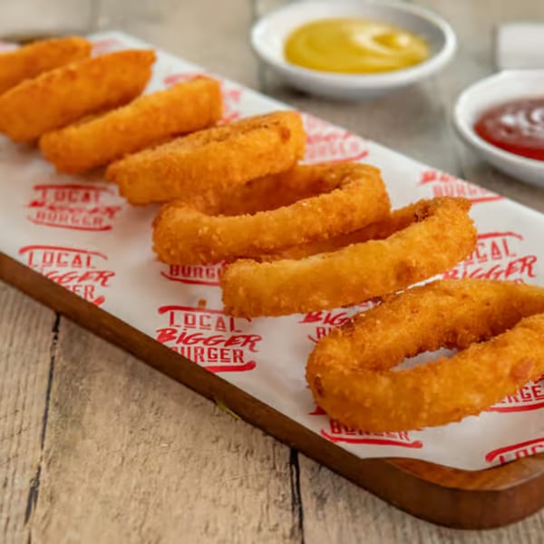 Crispy golden onion rings from Local Bigger Burger on a wooden board with dipping sauces.