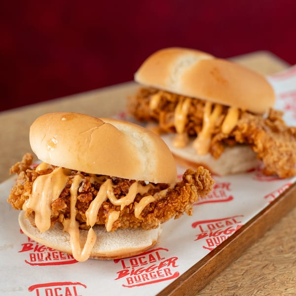 Two crispy chicken sandwiches with creamy sauce on branded paper from Local Bigger Burger.